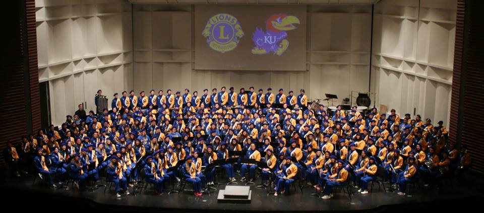 A wide, distant shot of the entire 180 student band from 2023 wearing their uniforms and sitting on the bandstand