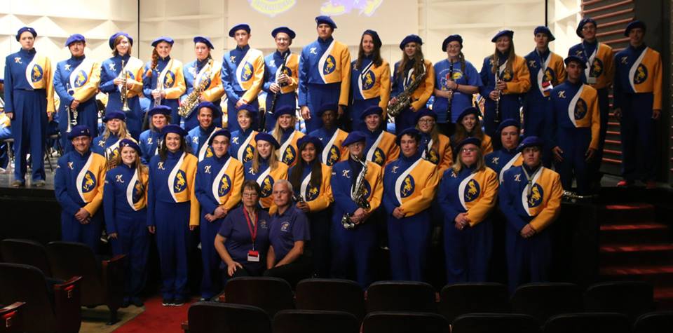 dozens of student musicians stand in three long rows all wearing their matching uniforms
